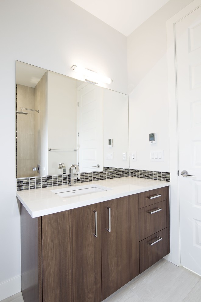 This is an example of a mid-sized contemporary 3/4 bathroom in Calgary with a drop-in sink, flat-panel cabinets, dark wood cabinets, engineered quartz benchtops, an alcove tub, a shower/bathtub combo, a one-piece toilet, gray tile, ceramic tile, grey walls and ceramic floors.