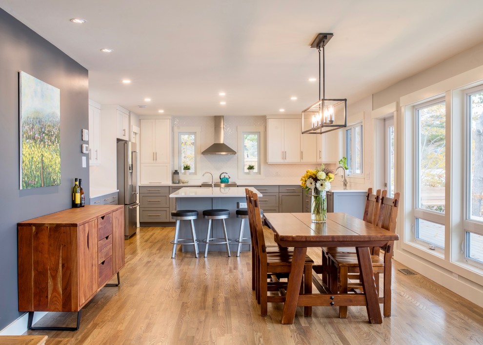 Transitional u-shaped medium tone wood floor and brown floor eat-in kitchen photo with shaker cabinets, gray cabinets, white backsplash, stainless steel appliances, an island and white countertops