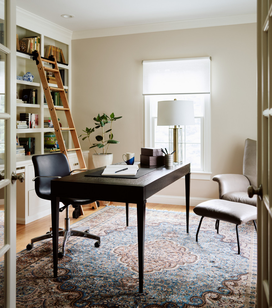 Mittelgroßes Klassisches Lesezimmer mit beiger Wandfarbe, hellem Holzboden und freistehendem Schreibtisch in Boston