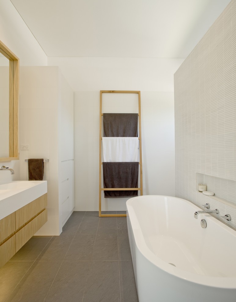 Large contemporary bathroom in Sydney with an integrated sink, flat-panel cabinets, light wood cabinets, solid surface benchtops, a freestanding tub, an alcove shower, a one-piece toilet, white tile, ceramic tile, white walls and limestone floors.