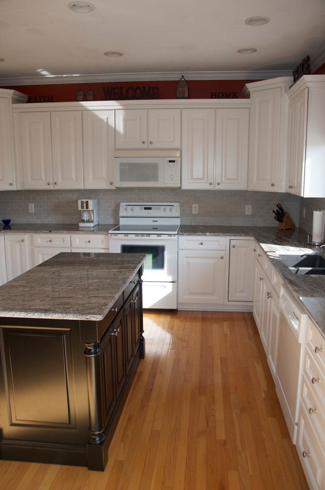 Example of a mid-sized transitional u-shaped medium tone wood floor kitchen design with an undermount sink, flat-panel cabinets, white cabinets, granite countertops, gray backsplash, subway tile backsplash, white appliances and an island