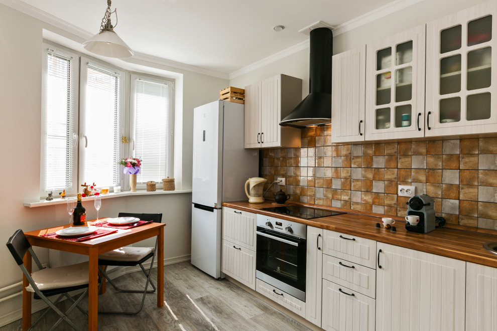 Photo of a traditional single-wall eat-in kitchen in Other with glass-front cabinets, beige cabinets, wood benchtops, multi-coloured splashback, white appliances, no island and brown floor.