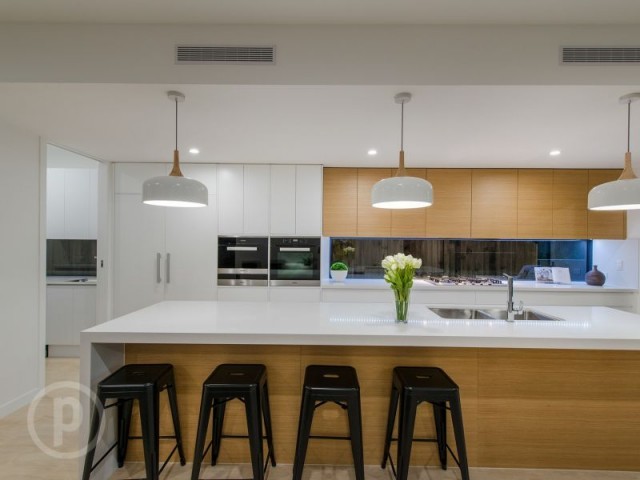 This is an example of a large contemporary galley eat-in kitchen in Brisbane with an undermount sink, medium wood cabinets, quartz benchtops, metallic splashback, glass sheet splashback, stainless steel appliances, light hardwood floors and with island.