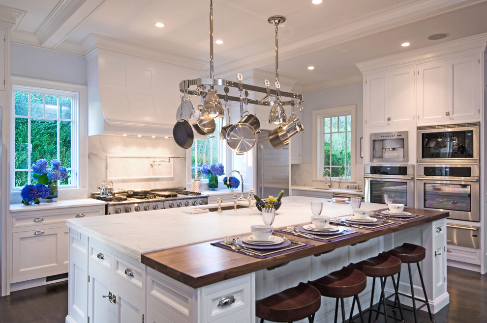 This is an example of a large beach style u-shaped eat-in kitchen in New York with an undermount sink, raised-panel cabinets, white cabinets, marble benchtops, white splashback, stone slab splashback, stainless steel appliances, dark hardwood floors and with island.