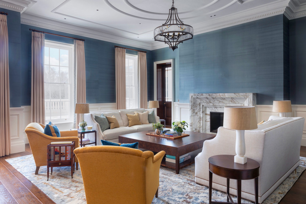 Traditional formal living room in Surrey with blue walls, medium hardwood floors, a standard fireplace, a stone fireplace surround, no tv, decorative wall panelling and wallpaper.