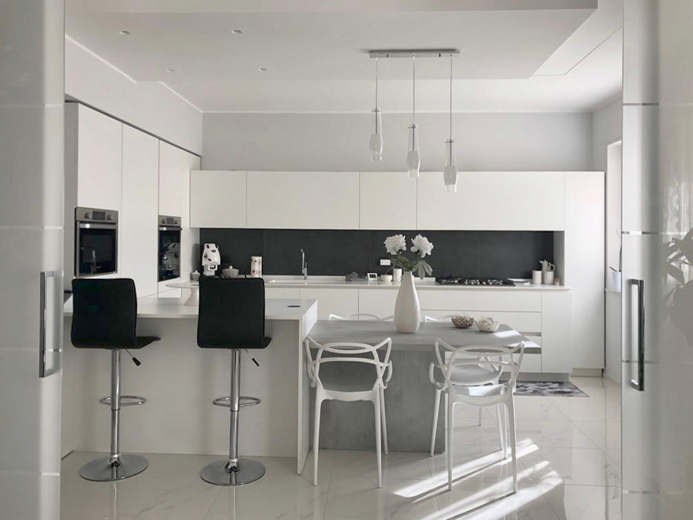 Mid-sized modern u-shaped open plan kitchen in Other with an integrated sink, flat-panel cabinets, white cabinets, solid surface benchtops, black splashback, porcelain splashback, stainless steel appliances, porcelain floors, a peninsula, white floor and white benchtop.
