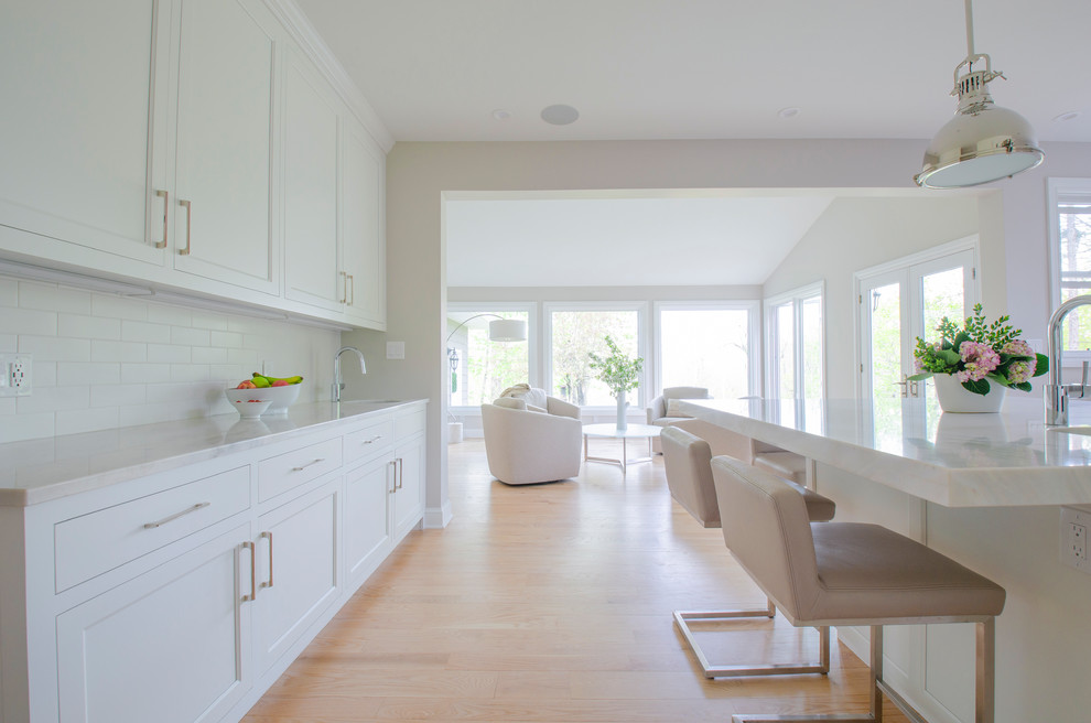 Inspiration for a large scandinavian u-shaped kitchen in Cleveland with an undermount sink, white cabinets, quartzite benchtops, white splashback, ceramic splashback, stainless steel appliances, light hardwood floors, with island and white benchtop.