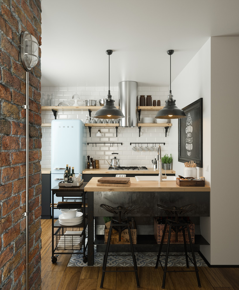 Mid-sized industrial galley open plan kitchen in Turin with flat-panel cabinets, black cabinets, wood benchtops, white splashback, coloured appliances, medium hardwood floors, a peninsula, subway tile splashback, a farmhouse sink and brown floor.