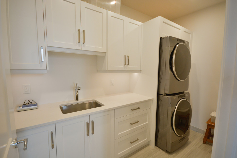 Inspiration for a mid-sized transitional single-wall dedicated laundry room remodel in Toronto with an undermount sink, shaker cabinets, white cabinets, quartz countertops, a stacked washer/dryer and white countertops