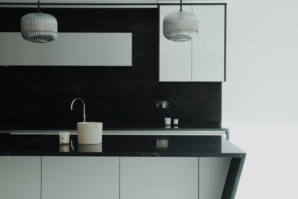 Design ideas for a large modern grey and black l-shaped kitchen/diner in Surrey with a built-in sink, flat-panel cabinets, grey cabinets, composite countertops, black splashback, engineered quartz splashback, black appliances, porcelain flooring, an island, white floors, black worktops, a coffered ceiling and feature lighting.