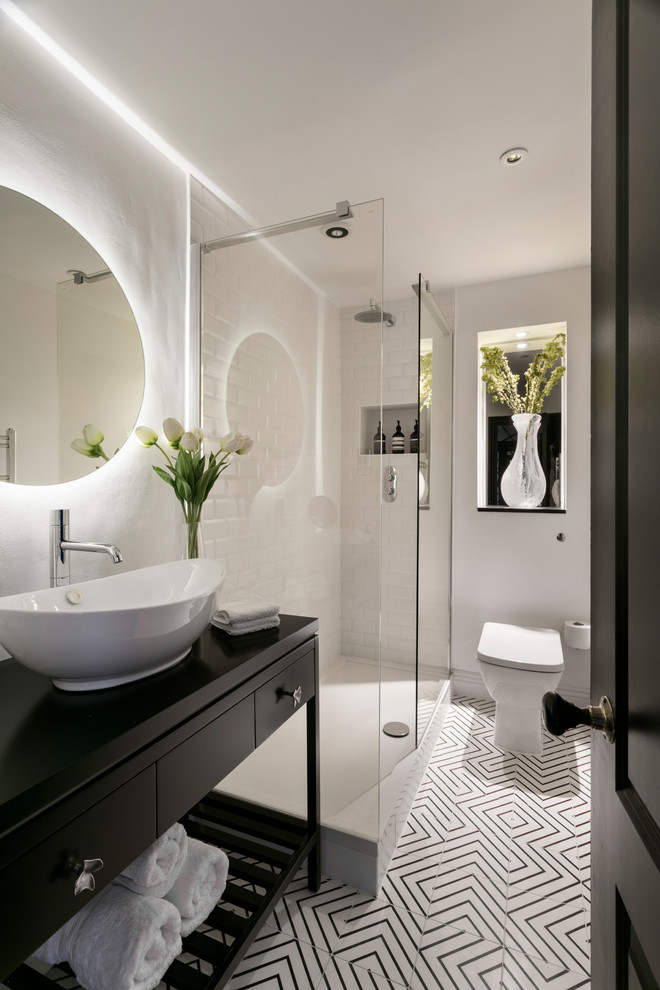 Inspiration for a small contemporary bathroom with flat-panel cabinets, black cabinets, an open shower, a one-piece toilet, white tile, subway tile, white walls, a vessel sink, white floor, an open shower and black benchtops.