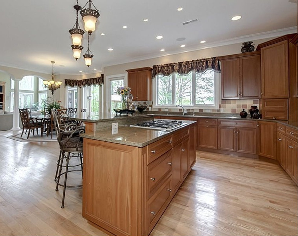 Huge transitional l-shaped limestone floor and beige floor enclosed kitchen photo in DC Metro with a double-bowl sink, recessed-panel cabinets, medium tone wood cabinets, granite countertops, multicolored backsplash, stainless steel appliances, a peninsula and ceramic backsplash