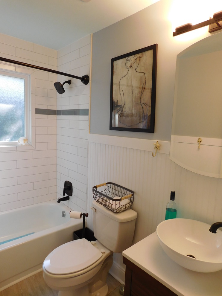 Photo of a small beach style master bathroom in Other with furniture-like cabinets, brown cabinets, an alcove tub, an alcove shower, a two-piece toilet, white tile, ceramic tile, grey walls, vinyl floors, a vessel sink, engineered quartz benchtops, brown floor and a shower curtain.
