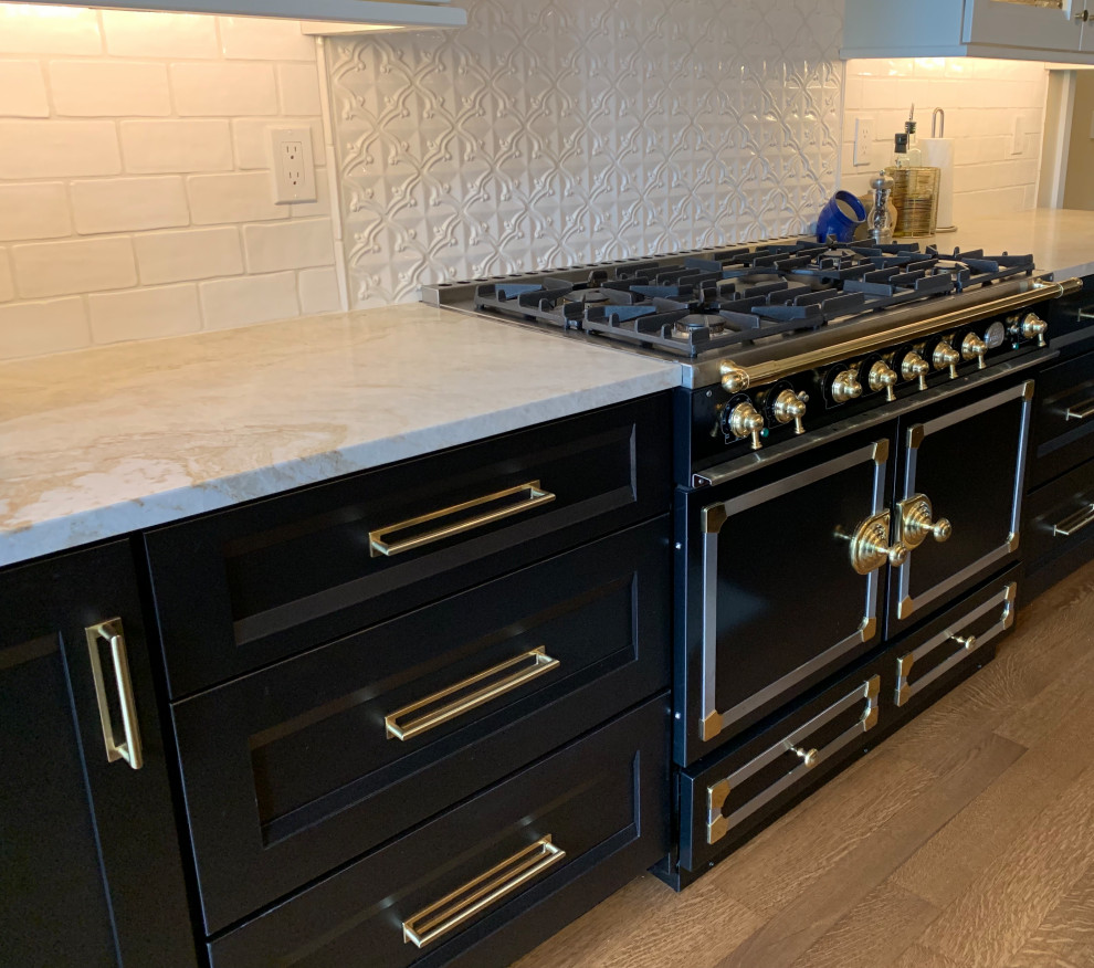 Design ideas for a large transitional l-shaped open plan kitchen in Milwaukee with an undermount sink, black cabinets, white splashback, ceramic splashback, black appliances, dark hardwood floors, with island and multi-coloured benchtop.