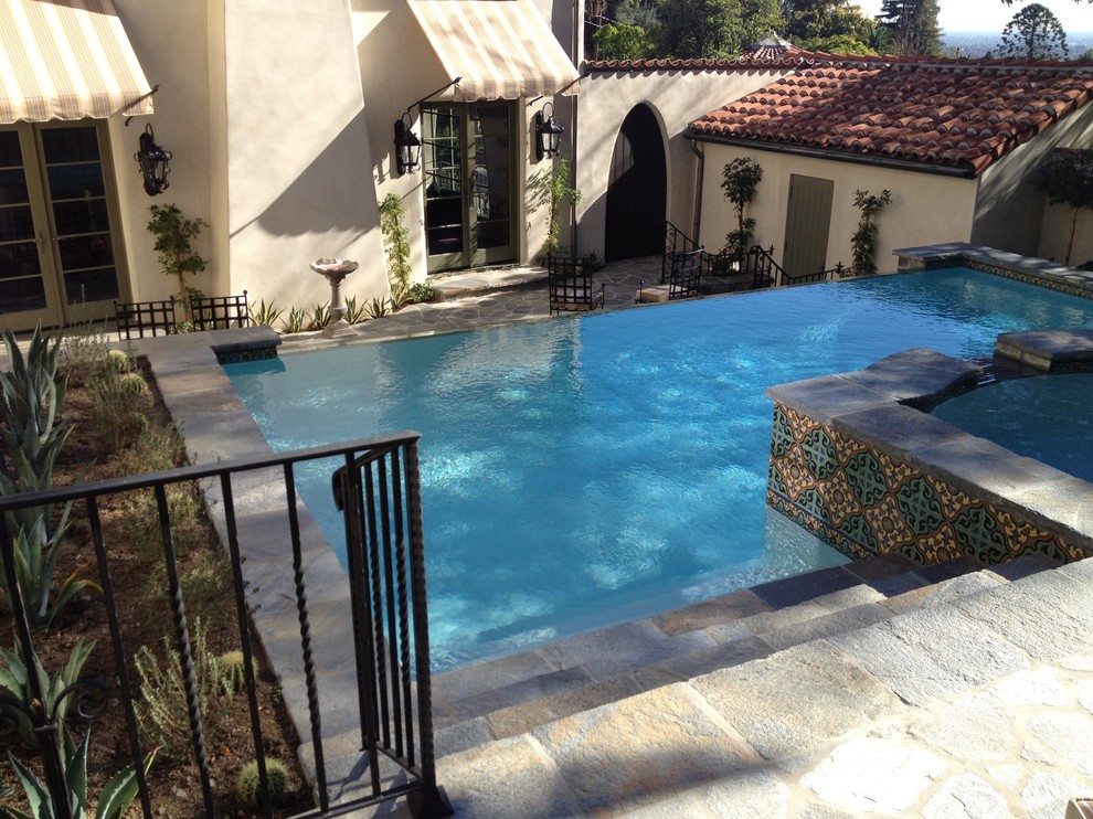Photo of a mid-sized mediterranean backyard custom-shaped infinity pool in Los Angeles with natural stone pavers.