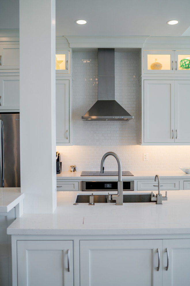 Mid-sized transitional galley medium tone wood floor and brown floor open concept kitchen photo with an undermount sink, beaded inset cabinets, white cabinets, solid surface countertops, white backsplash, porcelain backsplash, stainless steel appliances and an island