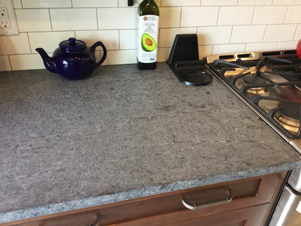 Inspiration for a mid-sized transitional l-shaped kitchen remodel in Ottawa with an undermount sink, shaker cabinets, dark wood cabinets, soapstone countertops, white backsplash, ceramic backsplash, stainless steel appliances and an island