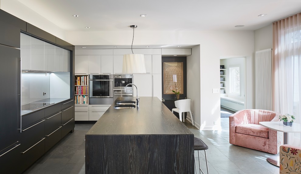 Photo of a mid-sized contemporary l-shaped open plan kitchen in Chicago with a double-bowl sink, flat-panel cabinets, wood benchtops, stainless steel appliances, black cabinets, with island, grey floor and black benchtop.