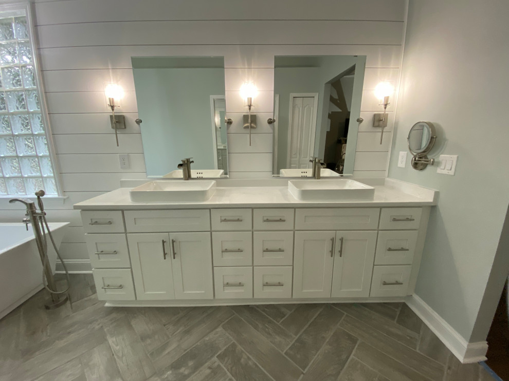 Design ideas for a large modern master bathroom in Jacksonville with shaker cabinets, white cabinets, a freestanding tub, a double shower, a one-piece toilet, white tile, subway tile, grey walls, wood-look tile, a vessel sink, granite benchtops, grey floor, a hinged shower door, white benchtops, a niche, a double vanity, a freestanding vanity, recessed and planked wall panelling.