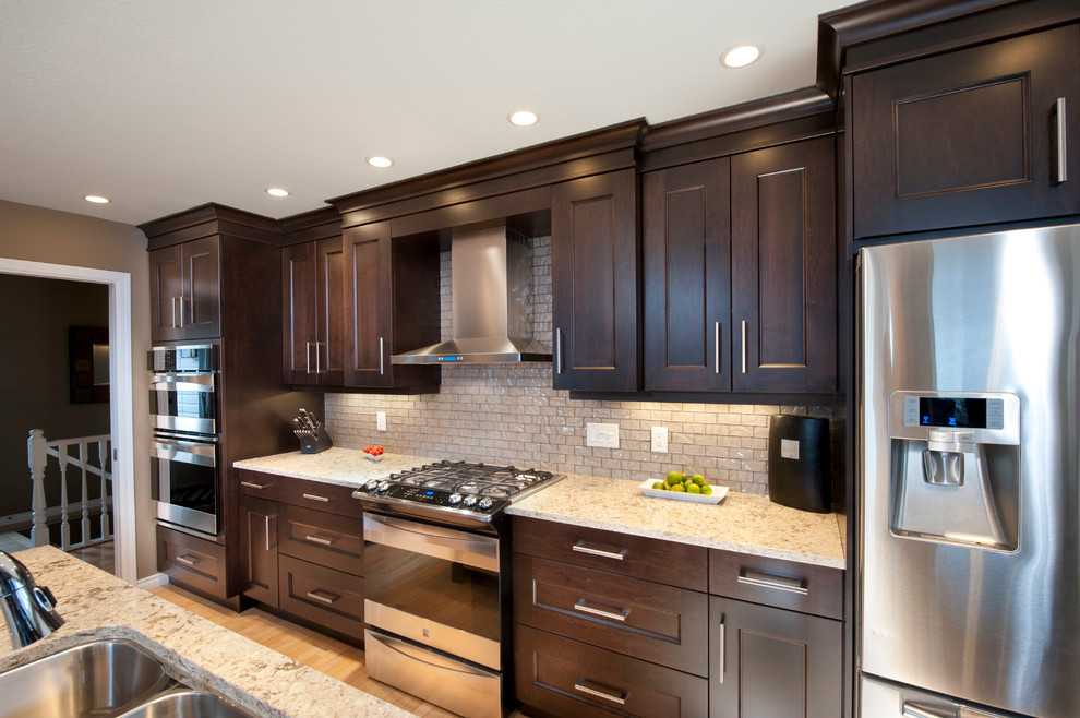 Inspiration for a large u-shaped light wood floor eat-in kitchen remodel in Vancouver with an undermount sink, recessed-panel cabinets, dark wood cabinets, glass tile backsplash, stainless steel appliances and an island