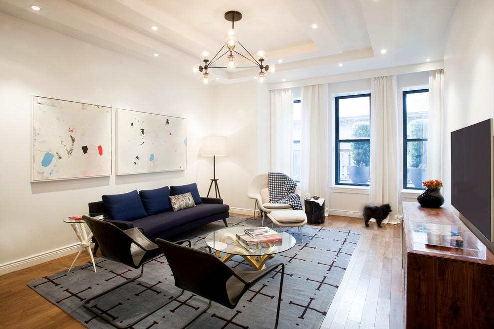 This is an example of a contemporary living room in New York with white walls, medium hardwood floors and a wall-mounted tv.