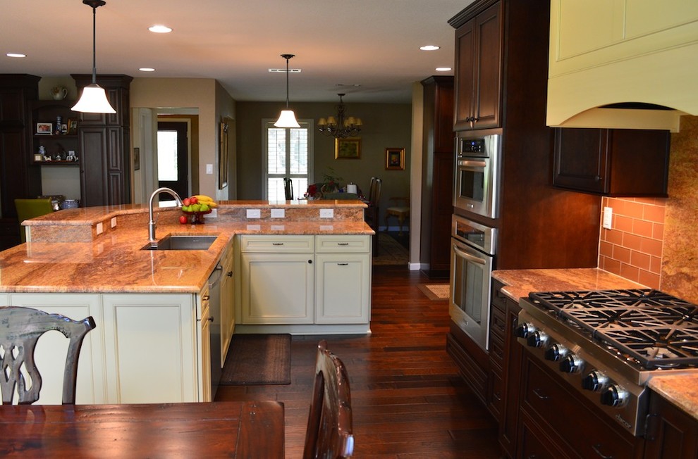 This is an example of a mid-sized transitional l-shaped eat-in kitchen in Austin with a drop-in sink, flat-panel cabinets, light wood cabinets, granite benchtops, orange splashback, glass tile splashback, stainless steel appliances and dark hardwood floors.