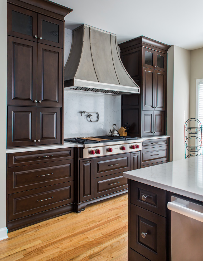 Inspiration for a large transitional l-shaped light wood floor open concept kitchen remodel in Atlanta with a farmhouse sink, raised-panel cabinets, dark wood cabinets, quartz countertops, white backsplash, stone slab backsplash, stainless steel appliances and an island