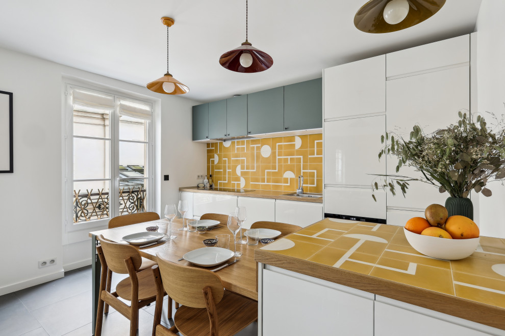 Inspiration for a scandinavian galley gray floor kitchen remodel in Paris with flat-panel cabinets, white cabinets, wood countertops, yellow backsplash, paneled appliances, a peninsula and brown countertops