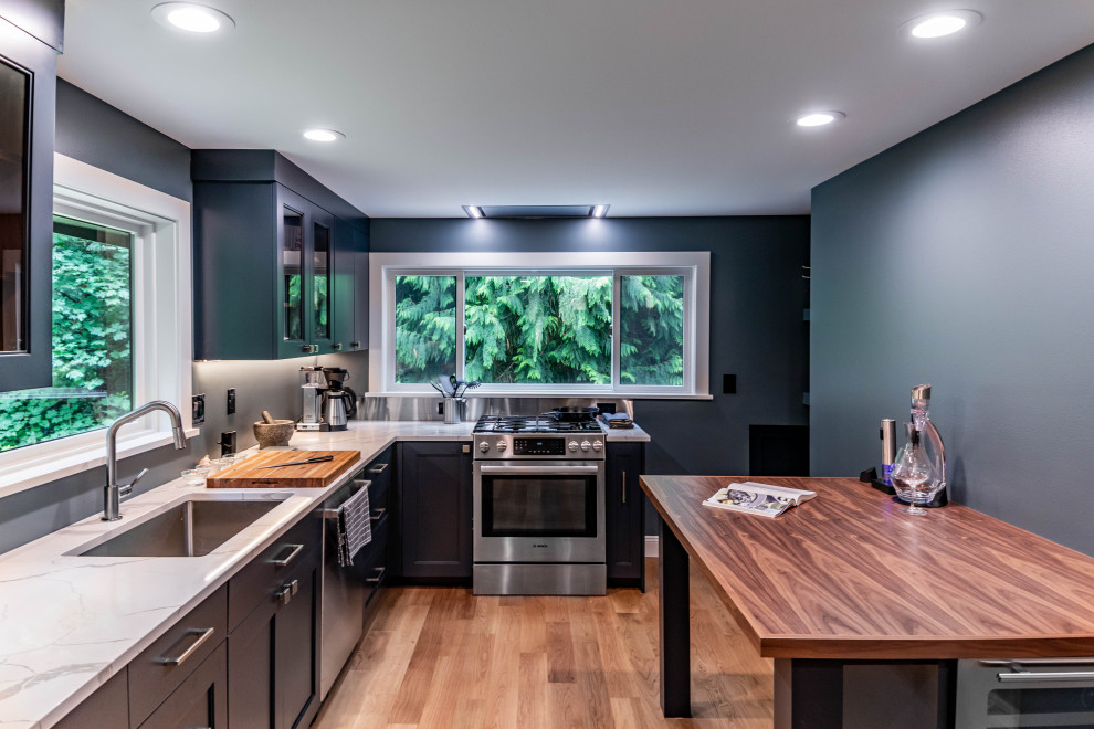 This is an example of a mid-sized transitional galley separate kitchen with a single-bowl sink, recessed-panel cabinets, blue cabinets, quartzite benchtops, grey splashback, cement tile splashback, stainless steel appliances, light hardwood floors, a peninsula, brown floor and white benchtop.