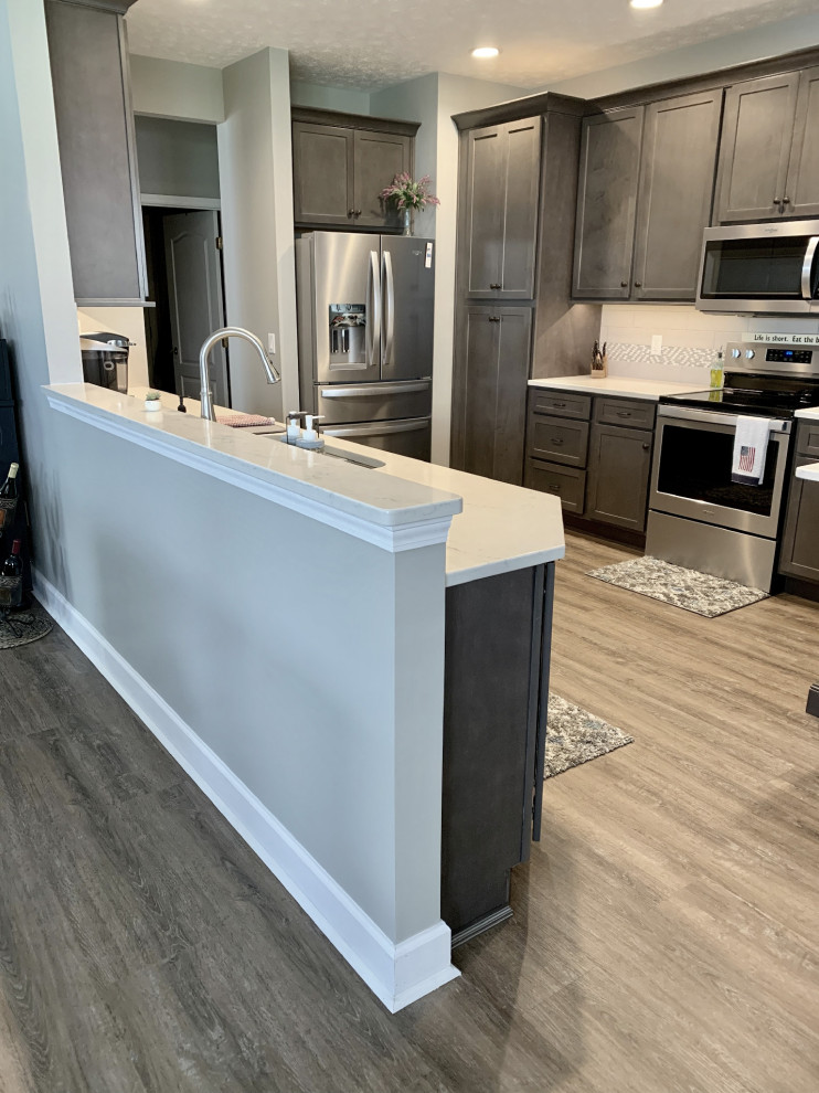 Large transitional u-shaped vinyl floor and gray floor open concept kitchen photo with an undermount sink, shaker cabinets, gray cabinets, quartz countertops, gray backsplash, ceramic backsplash, stainless steel appliances, a peninsula and white countertops