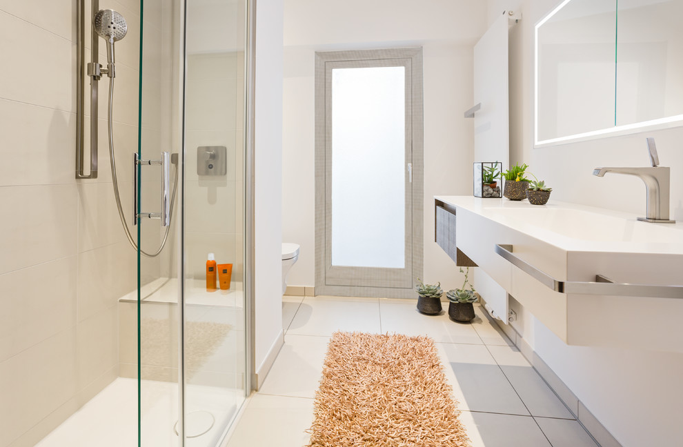 Photo of a small contemporary 3/4 bathroom in Cologne with flat-panel cabinets, beige tile, white walls, beige floor, a sliding shower screen, a wall-mount toilet, brown cabinets, a curbless shower, ceramic tile, ceramic floors, a console sink and solid surface benchtops.