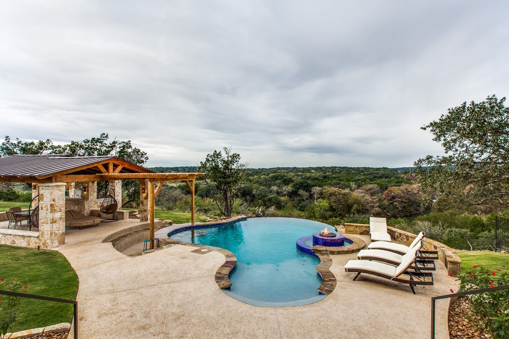 Inspiration for an expansive transitional backyard custom-shaped infinity pool in Austin with a water feature and stamped concrete.