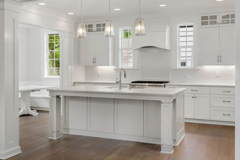 Inspiration for a large traditional l-shaped eat-in kitchen in Los Angeles with a farmhouse sink, shaker cabinets, white cabinets, quartz benchtops, white splashback, subway tile splashback, stainless steel appliances, light hardwood floors, with island, beige floor and white benchtop.
