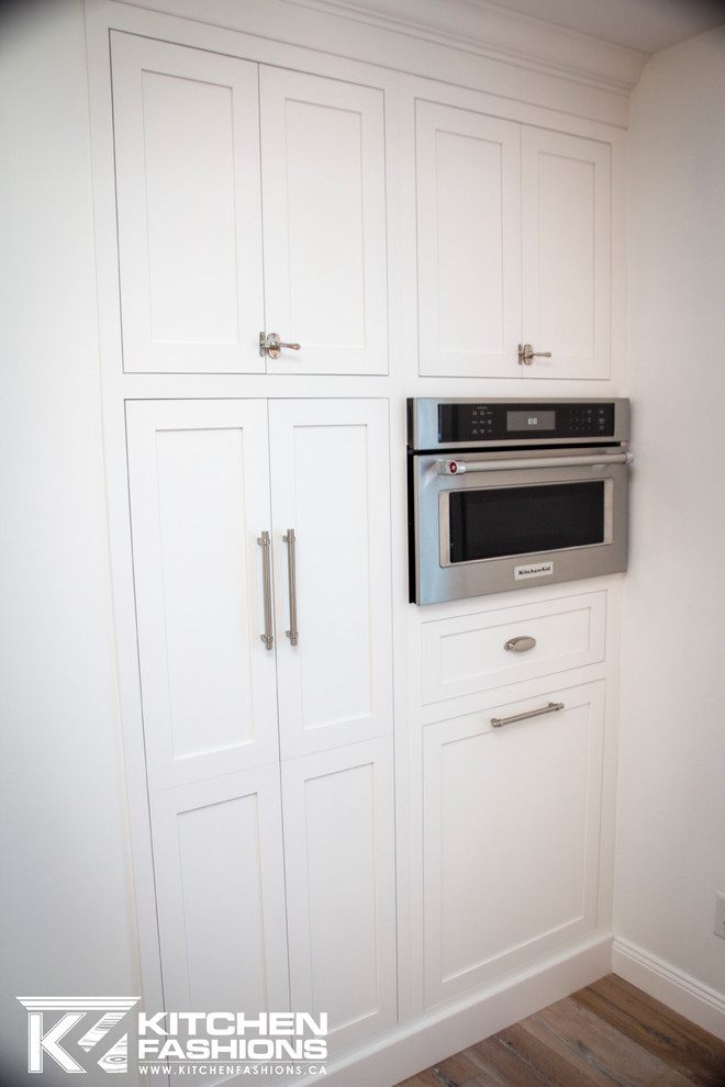 Eat-in kitchen - large transitional u-shaped light wood floor eat-in kitchen idea with a farmhouse sink, shaker cabinets, white cabinets, granite countertops, white backsplash, subway tile backsplash, stainless steel appliances and no island