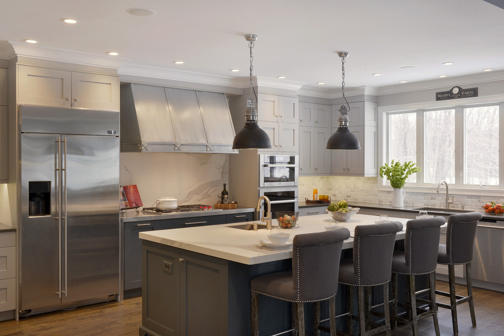 Photo of an expansive traditional l-shaped open plan kitchen in New York with an undermount sink, shaker cabinets, grey cabinets, white splashback, stainless steel appliances, medium hardwood floors and with island.