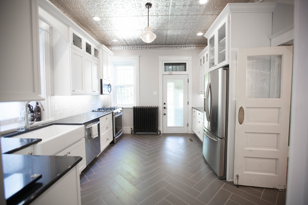 This is an example of a mid-sized traditional u-shaped separate kitchen in St Louis with a farmhouse sink, shaker cabinets, white cabinets, stone tile splashback, granite benchtops, white splashback, stainless steel appliances, vinyl floors and no island.