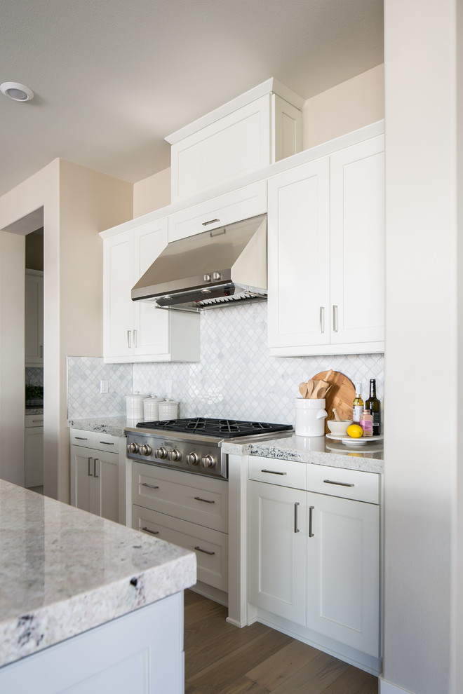 This is an example of a transitional l-shaped open plan kitchen in San Diego with white cabinets, granite benchtops, white splashback, stainless steel appliances, medium hardwood floors and with island.
