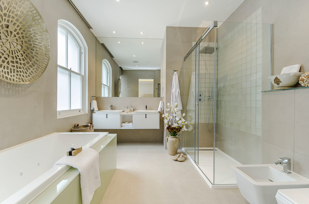 Photo of a contemporary master bathroom in London with flat-panel cabinets, white cabinets, a drop-in tub, a bidet, beige tile, beige walls, beige floor, a sliding shower screen and white benchtops.