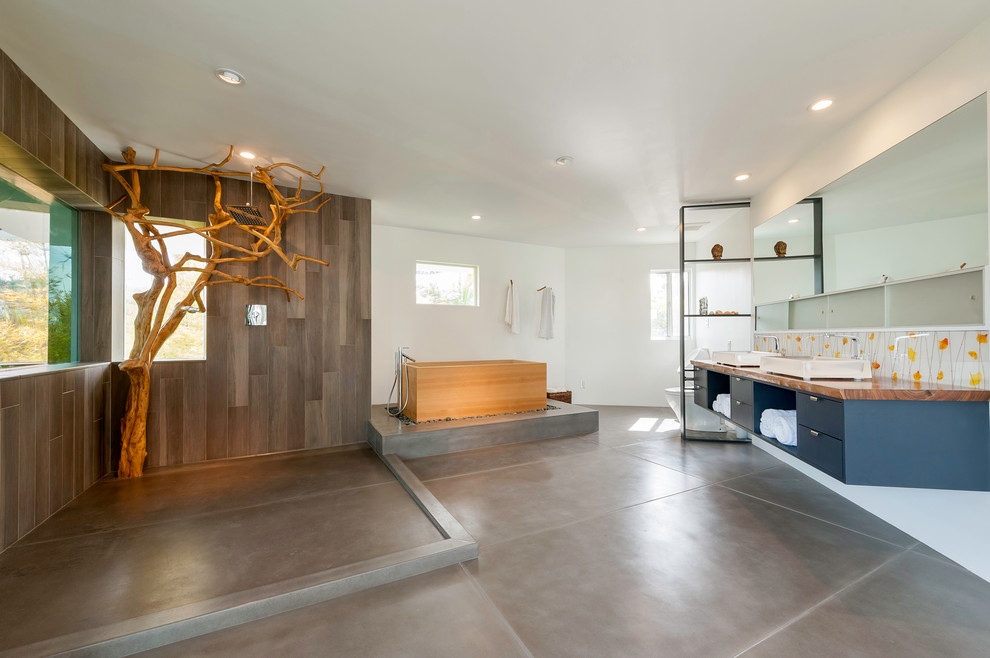 Expansive asian master bathroom in San Diego with flat-panel cabinets, black cabinets, a japanese tub, an open shower, a one-piece toilet, gray tile, cement tile, white walls, concrete floors, a trough sink, wood benchtops, grey floor and an open shower.
