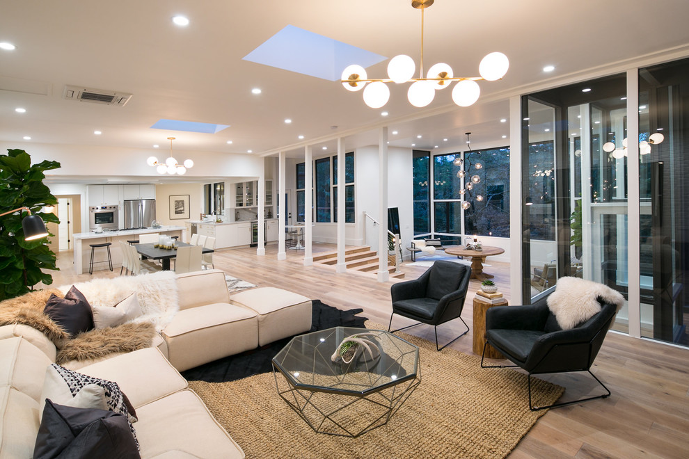 This is an example of a large midcentury open concept family room in San Francisco with white walls, light hardwood floors, a standard fireplace, a concrete fireplace surround and white floor.