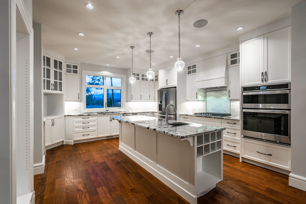 Large transitional u-shaped dark wood floor and brown floor eat-in kitchen photo with an undermount sink, recessed-panel cabinets, white cabinets, granite countertops, white backsplash, ceramic backsplash, stainless steel appliances, an island and multicolored countertops