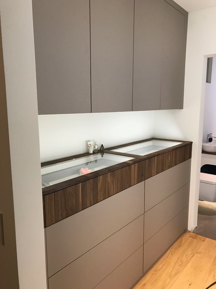 Mid-sized contemporary gender-neutral dressing room in Dusseldorf with flat-panel cabinets, beige cabinets, medium hardwood floors and brown floor.