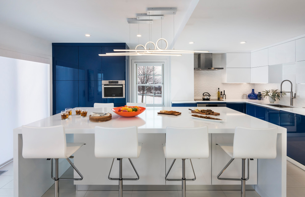Photo of a large bohemian l-shaped kitchen/diner in Boston with a submerged sink, flat-panel cabinets, blue cabinets, engineered stone countertops, white splashback, ceramic splashback, coloured appliances, an island, white floors and white worktops.