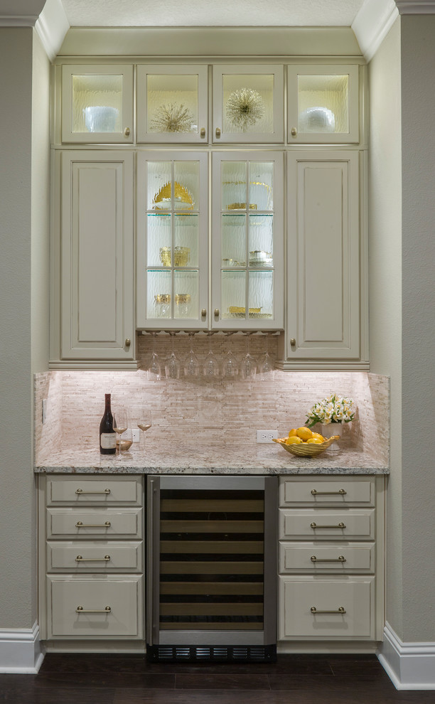 Photo of a small transitional single-wall wet bar in Los Angeles with raised-panel cabinets, beige cabinets, granite benchtops, beige splashback, stone tile splashback, dark hardwood floors, brown floor and grey benchtop.