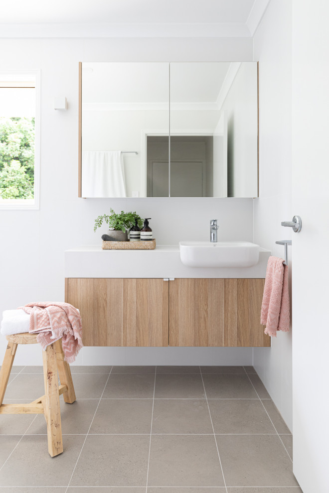 This is an example of a mid-sized beach style master bathroom in Brisbane with flat-panel cabinets, light wood cabinets, an open shower, a one-piece toilet, white tile, porcelain tile, white walls, porcelain floors, engineered quartz benchtops, grey floor, an open shower, white benchtops, a single vanity and a floating vanity.