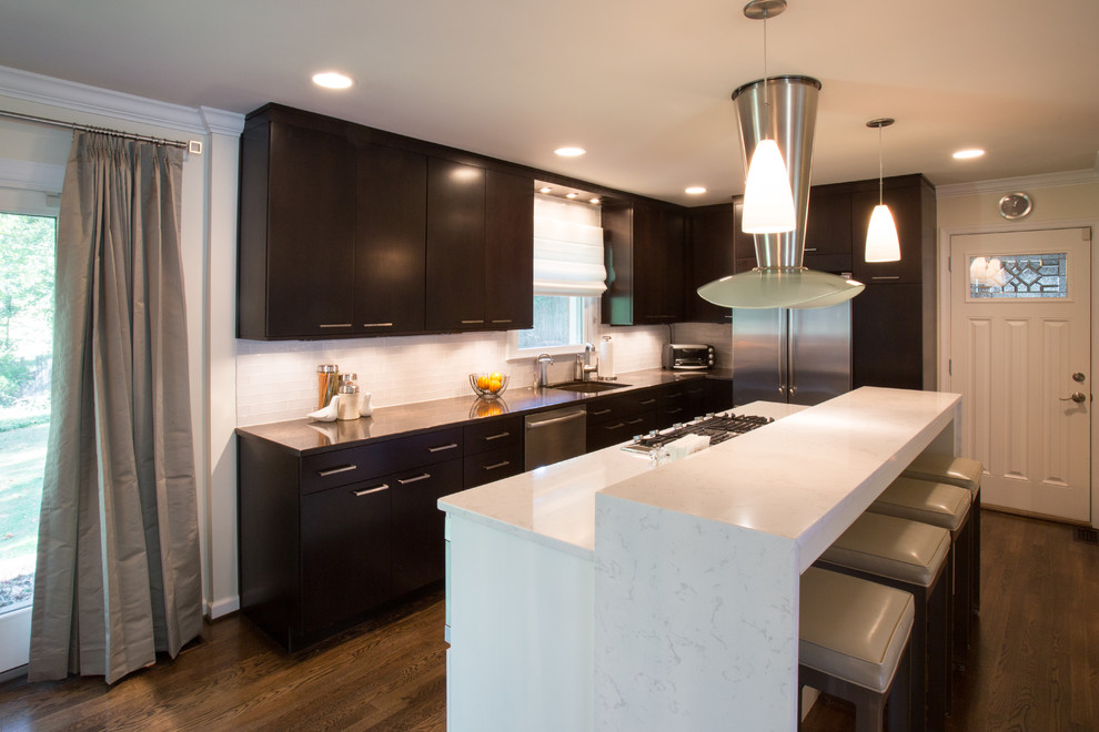 This is an example of a modern l-shaped open plan kitchen in DC Metro with an undermount sink, flat-panel cabinets, dark wood cabinets, quartz benchtops, white splashback, ceramic splashback, stainless steel appliances, dark hardwood floors and with island.