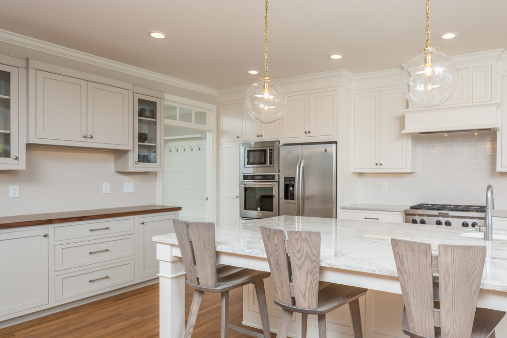 Inspiration for a large transitional u-shaped medium tone wood floor and brown floor eat-in kitchen remodel in Raleigh with a farmhouse sink, shaker cabinets, white cabinets, white backsplash, stainless steel appliances, an island, quartzite countertops, subway tile backsplash and white countertops