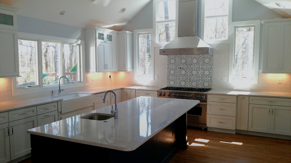 Inspiration for a mid-sized contemporary l-shaped eat-in kitchen in Baltimore with a farmhouse sink, white splashback, ceramic splashback, stainless steel appliances, light hardwood floors, with island, beaded inset cabinets, white cabinets and granite benchtops.