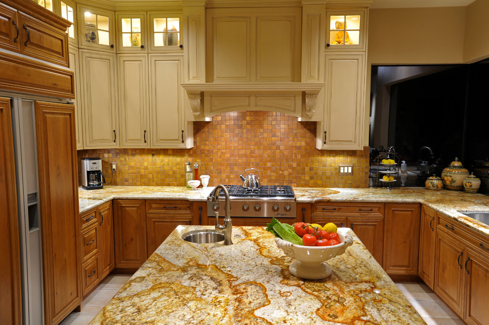 Example of a transitional ceramic tile kitchen design with an undermount sink, raised-panel cabinets, distressed cabinets, granite countertops, metallic backsplash, metal backsplash, paneled appliances and an island