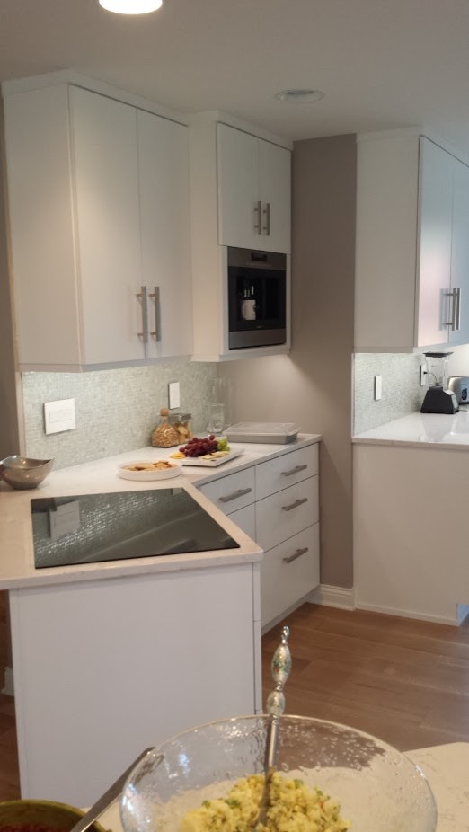 Example of a small transitional galley medium tone wood floor enclosed kitchen design with an undermount sink, flat-panel cabinets, white cabinets, quartz countertops, white backsplash, mosaic tile backsplash, stainless steel appliances and a peninsula